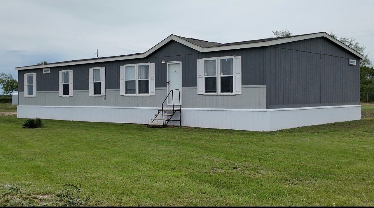 Gray manufactured home with white trim, front steps and a grassy yard.